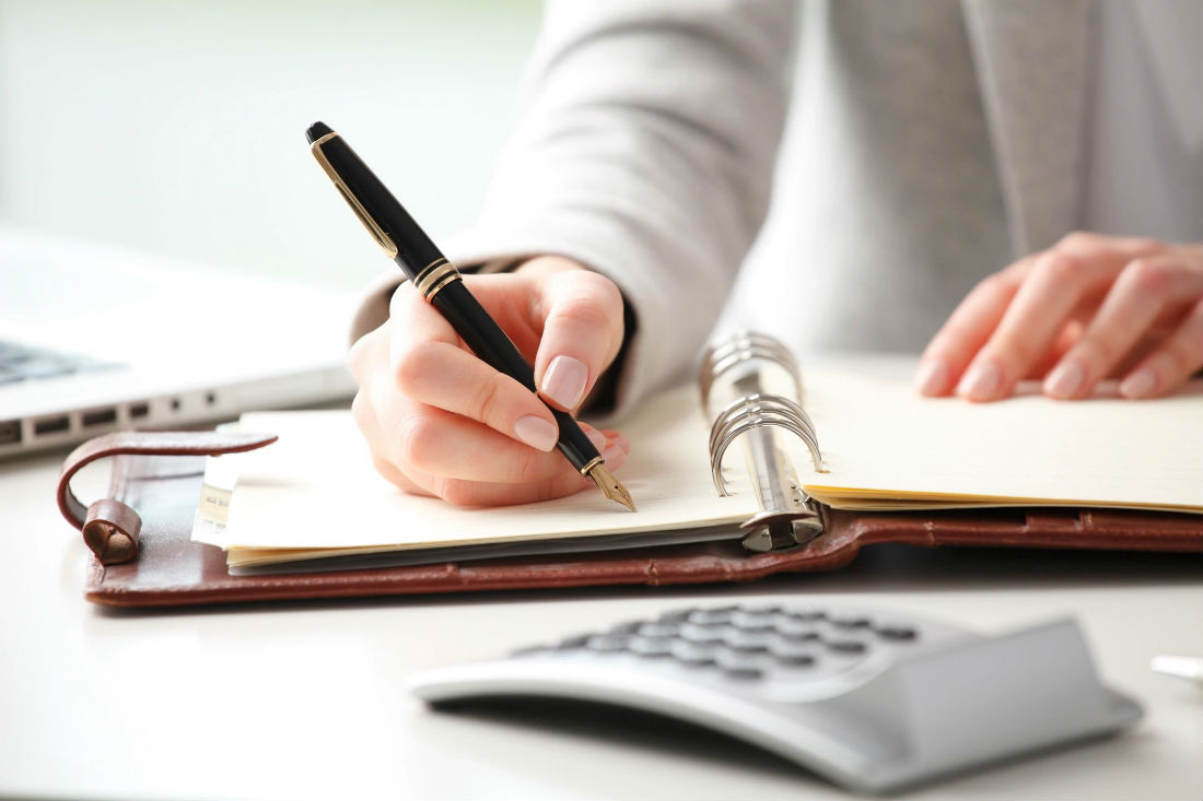 A person writing in a notebook with a pen.